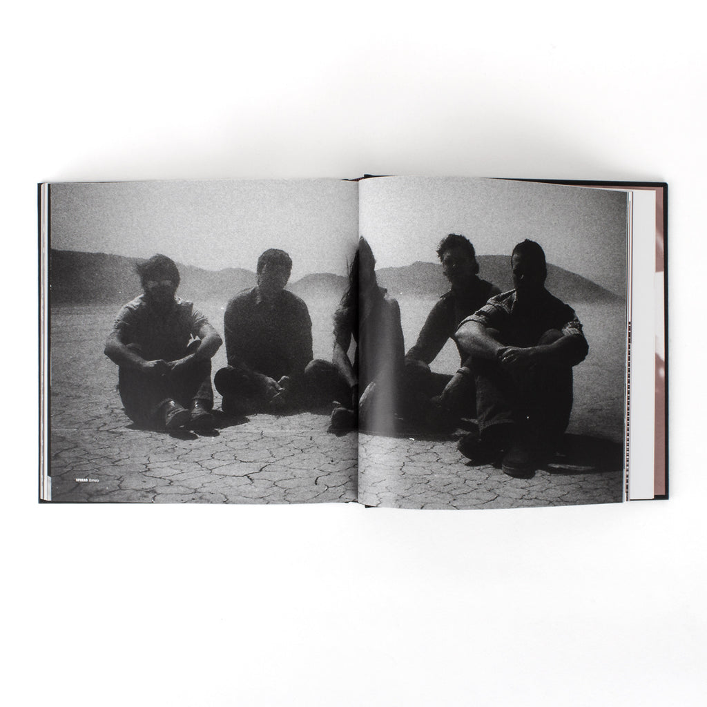 image of an open book on a white background. book pages show a black and white image taking up both pages of five men sitting in the desert