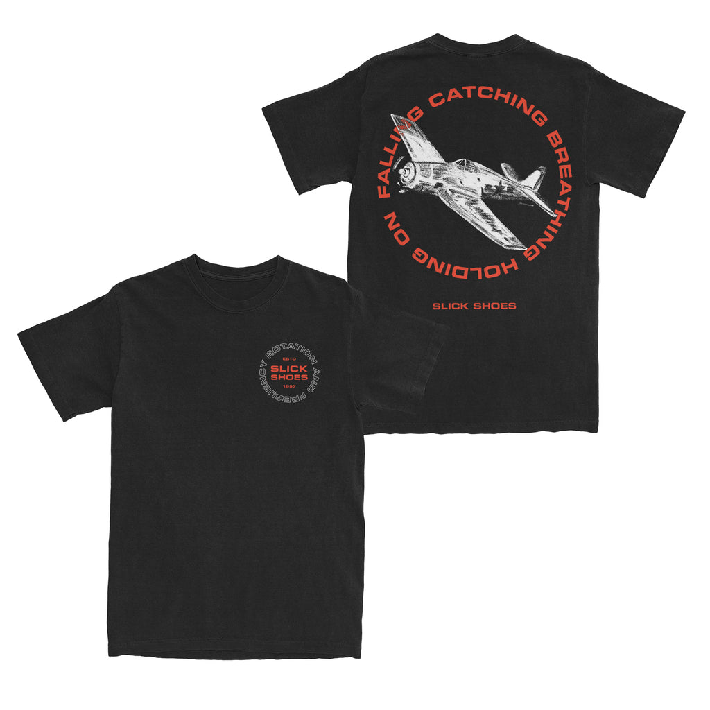 image of the front and back of a black tee shirt on a white background. the front of the tee is on the right and has a small chest print on the right that says in red slick shoes with a circle of white outline text around it that says rotation and frequency. the back of te tee is on the right and has a full back print. in the center in white is an airplane with red text around it that says falling catching breathing holding on and then slick shoes at the bottom