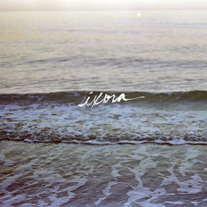 image of an album cover. cover is of waves on a beach. it white in the center says ixora