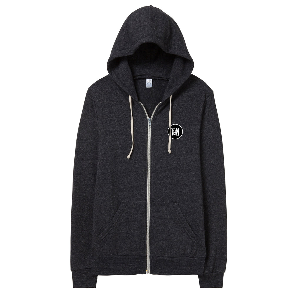 image of an eco black zip up hoodie on a white background. there is a small print on the right chest of a black circle with a white outline, and white text on the inside that says T & N