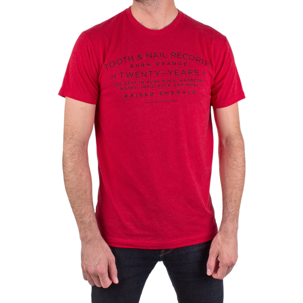 image of a white man from the down wearing a red tee shirt and black jeans. the front of the tee shirt has a print across the chest in black that says tooth & Nail records, born orange, twenty-years, the best in punk rock, hardcore, metal, indie rock and more. raised emerald